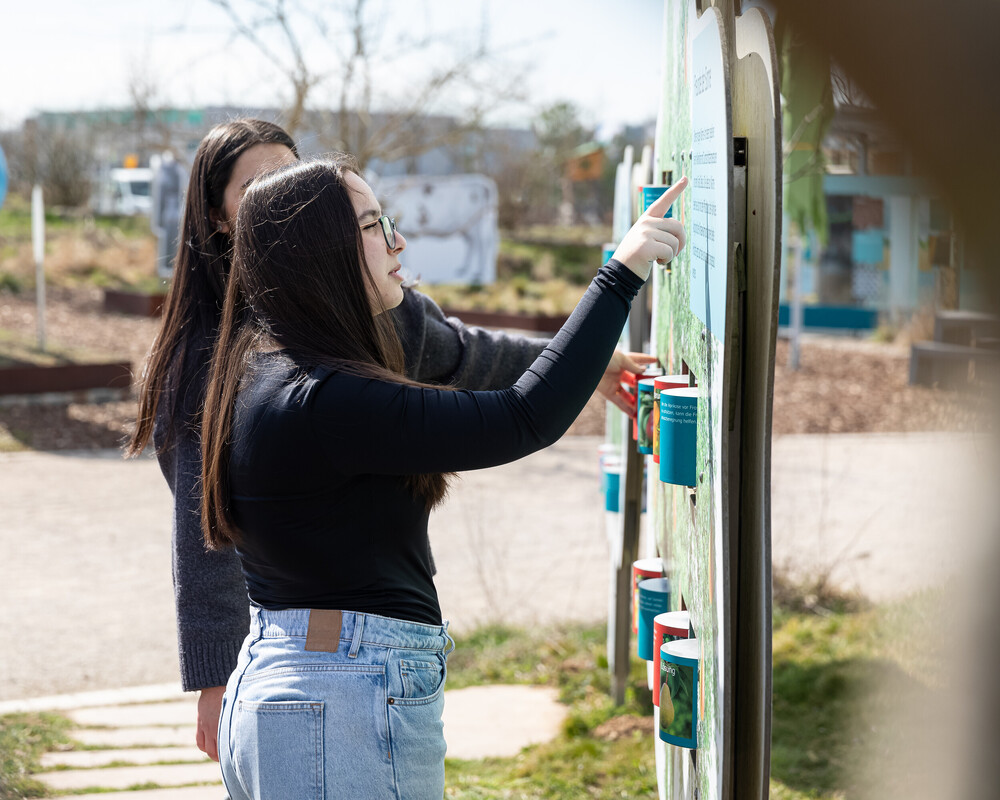 Sch&uuml;lerinnen bei einer schauen sich Ausstellungsstation im Au&szlig;enbereich der KLIMA ARENA an.